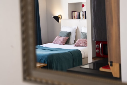 Chambre moderne à La Tour Grégoire à Clermont-Ferrand avec tête de lit blanche, coussins colorés et vue sur la ville