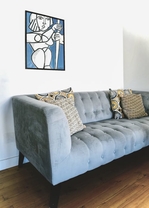 Canapé gris capitonné avec coussins à motifs sous une œuvre d'art abstraite moderne à l'hôtel boutique La Tour Grégoire
