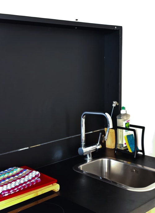 Évier de cuisine noir moderne avec robinetterie chromée, torchons colorés et produits de nettoyage à La Tour Grégoire BnB