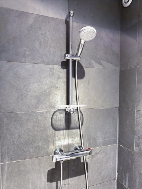 Douche moderne avec pommeau chromé effet pluie et douchette manuelle sur carrelage gris, hôtel La Tour Grégoire