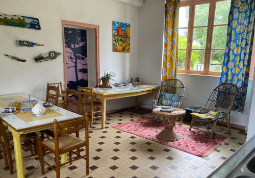 Bright cottage interior at Le Lama Zébré with dining table, desk, wicker chairs, and colorful African-inspired décor near