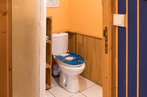 Bathroom with white toilet and blue floral seat cover, wooden wainscoting, yellow walls in Fisher Sheep Cottage at Le Lama