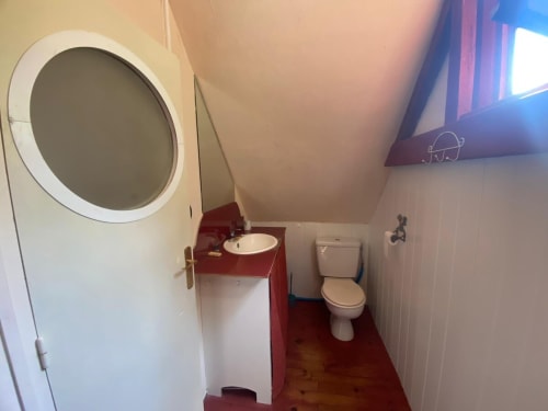 Compact bathroom in The Fisher Sheep Cottage at Le Lama Zébré with red accents, circular porthole window, sink, and toilet