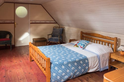 Cozy cottage bedroom at Le Lama Zébré in Penmarch with wooden bed, blue bedding, and garden views