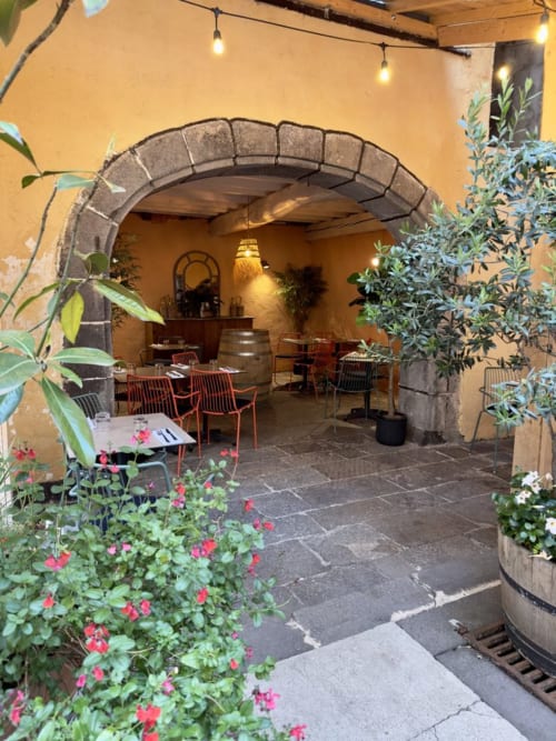 Cour enchanteresse avec arcade à l'entrée de la Maison d'hôtes La Tour Grégoire à Clermont-Ferrand, ornée de plantes fleuries et tables de restaurant