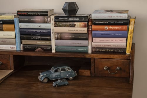 Bureau en bois avec des livres français empilés, vase géométrique noir et petites voitures bleues vintage à l'hôtel-boutique La Tour Grégoire