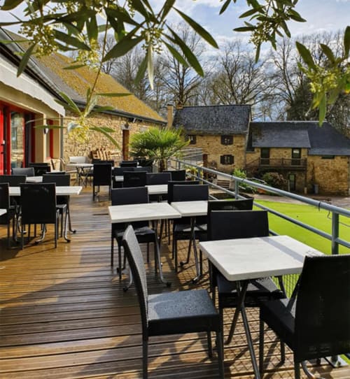 Terrasse de restaurant en plein air de la Résidence hôtelière du Coiroux à Aubazine avec chaises noires, tables blanches et bâtiments en pierre