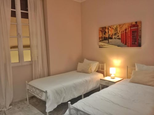 Dormitorio doble en apartamento de Jerez de la Frontera con camas blancas, lámpara de mesita, ventana con cortinas y cabina telefónica roja