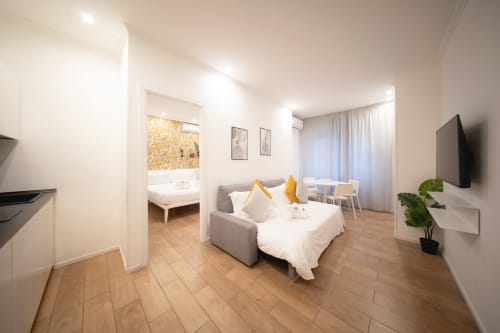 Camera moderna all'IV House BnB di Roma con divano letto grigio, cuscini gialli e bagno ensuite visibile