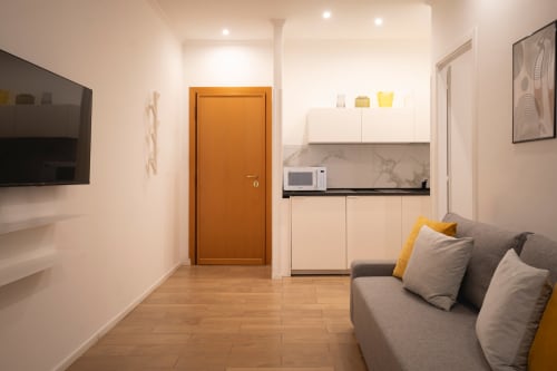 Camera moderna in IV House Rome BnB con angolo cottura, divano grigio e porta arancione