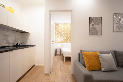 Moderno monolocale a IV House Roma con divano grigio, angolo cottura e camera da letto con dettagli gialli