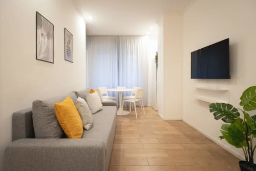 Soggiorno moderno della IV House Roma B&B con divano grigio, dettagli gialli e TV a parete