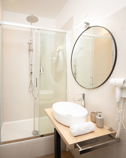 Bagno moderno presso IV House Roma con specchio rotondo, lavabo a bacinella e cabina doccia in vetro