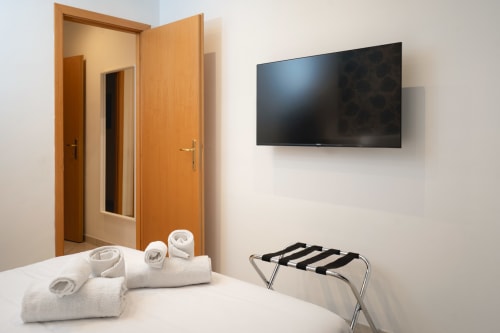 Camera del IV House Rome BnB con porte in legno, TV a schermo piatto, asciugamani arrotolati e portabagagli