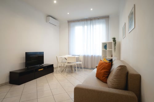 Moderno monolocale a IV House Roma con divano beige, TV, zona pranzo e luminose finestre
