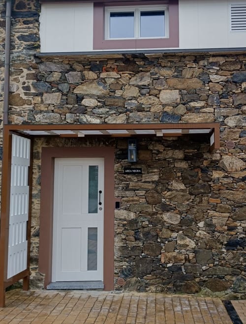 Entrada con fachada de piedra al apartamento Area Negra en Casa Rural San Andrés de Teixido, Galicia, con puerta blanca y porche de madera