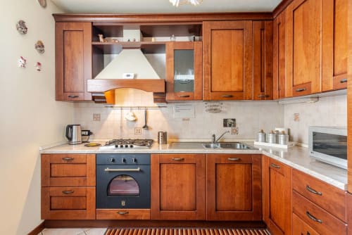 "Classic solid wood kitchen from Casa Meravigliosa in Fontanafredda, complete with a black fan oven, gas hob, chimney hood, and microwave on a light-colored countertop."