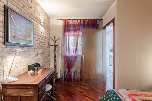 "Bedroom at Casa Meravigliosa in Fontanafredda with exposed brick walls, an antique wooden desk, dark parquet floors, and a classic, rustic-style coat rack."