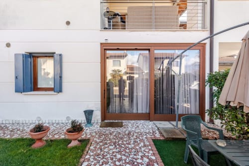 "Detached entrance to Casa Meravigliosa in Fontanafredda with large mosaic patio, manicured lawn, terracotta pots, and wooden French windows overlooking the upper balcony."