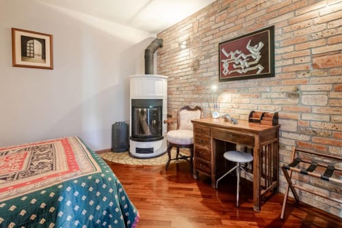 "Cozy bedroom at Casa Meravigliosa in Fontanafredda with a modern wood-burning stove, exposed brick wall, classic wooden armchair, and parquet flooring."