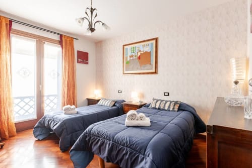 "Second bedroom at Casa Meravigliosa in Fontanafredda with two single beds, blue duvets, classic wooden bedside tables, and decorative paintings on the wall with light-colored wallpaper."