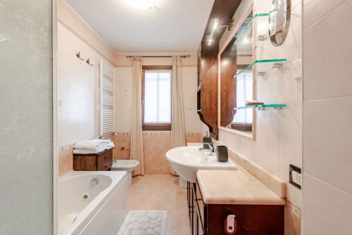 "Large bathroom at Casa Meravigliosa in Fontanafredda with a white whirlpool bathtub, a dark wood vanity sink with a marble top, a bidet, and a white radiator."