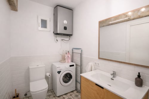 Baño moderno con azulejos blancos tipo metro, lavadora, tocador con lavamanos, inodoro y toallero eléctrico en apartamento de Mérida