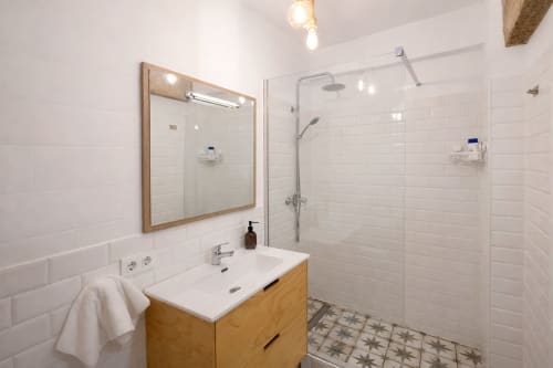 Baño moderno en apartamento de Mérida con vanidorio de madera, azulejos blancos tipo metro, ducha con mampara de vidrio y piso decorativo