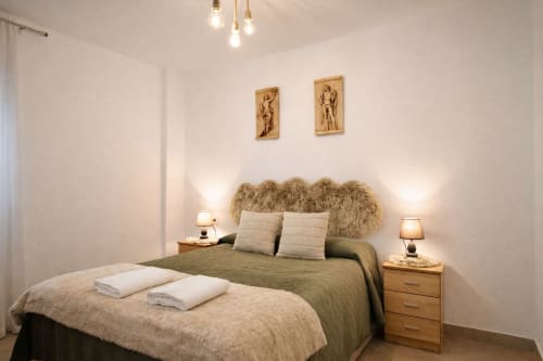Recámara moderna en Mérida con ropa de cama verde, cabecera tapizada, lámparas colgantes y mesas de noche de madera