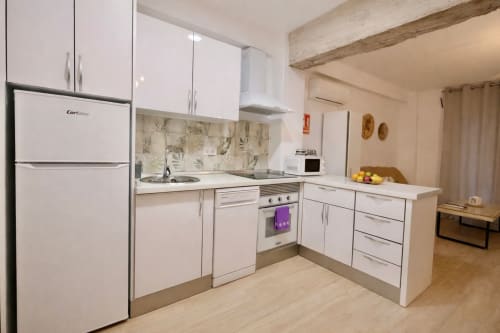 Cocina blanca moderna con electrodomésticos de acero inoxidable y vigas de madera vista en departamento de Mérida