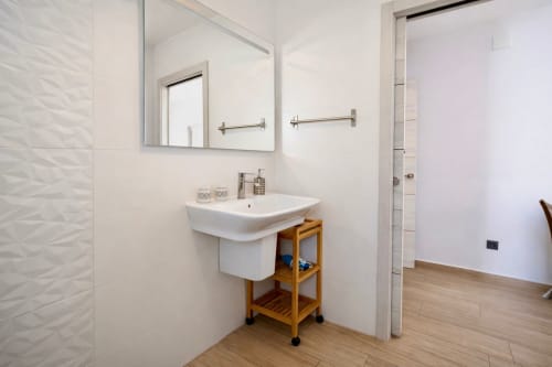Baño moderno en apartamento de Mérida con lavamanos blanco, vanidad de madera, espejo y azulejos texturizados