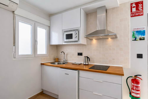 Cocina moderna blanca con encimera de madera, electrodomésticos de acero inoxidable y salpicadero de azulejos beige en apartamento de Mérida