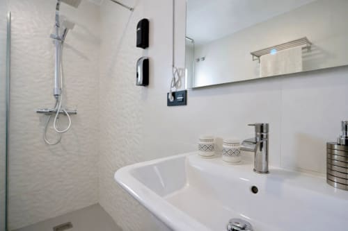 Baño moderno con lavabo blanco, grifo cromado y ducha con mampara de cristal en apartamento Gestyp-AT en Mérida
