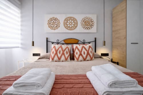 Dormitorio de apartamento moderno en Mérida con arte decorativo en pared, almohadas estampadas y toallas enrolladas en la cama