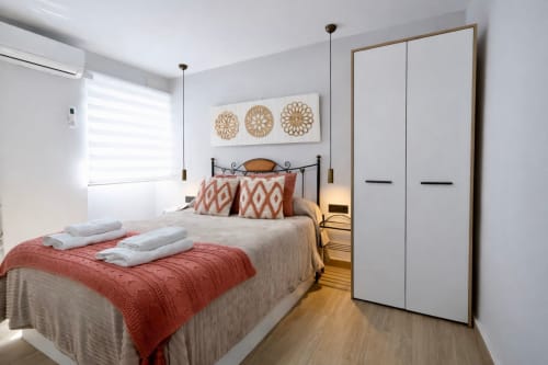 Habitación moderna del apartamento Gestyp-AT en Mérida con cama queen, detalles coralinos, armario blanco y vista a la ciudad