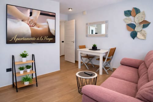 Moderno apartamento en Mérida con sofá rosa, escritorio de trabajo, plantas y cartel de masaje spa en la pared