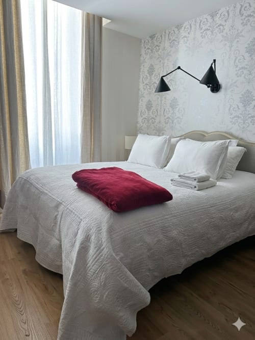 Chambre moderne à L'Alombre BnB à Lectoure avec literie blanche matelassée, jeté bordeaux, appliques murales noires et motifs