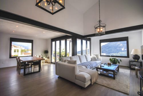 Suite de hotel moderno con sala de estar abierta, comedor, ventanales con marcos negros con vistas a las montañas, muebles beige y