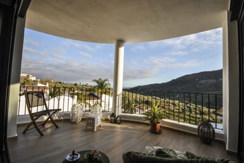Modern hotel balcony overlooking Mediterranean hills with panoramic views, comfortable seating, and lush vegetation in Spain