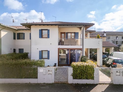 "Exterior of Casa Meravigliosa in Fontanafredda: a modern terraced house with a white facade, blue shutters, a furnished balcony, and a private entrance with a private garden."