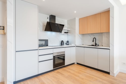 Modern kitchen in Marbella apartment with white cabinetry, marble backsplash, black appliances, and wooden upper cabinets