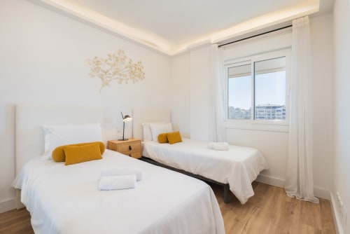 Modern twin bedroom in Marina Banús apartment with city views, white bedding, and mustard accents