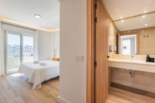 Modern bedroom with wooden bathroom en-suite, city views from balcony at Marina Banús apartment in Marbella