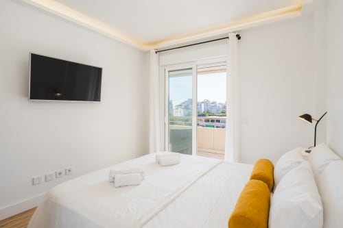 Modern bedroom at Marbella Home Rentals with city views, balcony, flat-screen TV, and white linens in Puerto Banús