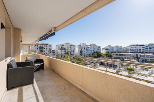 Spacious balcony at Marbella Home Rentals Marina Banús with city views, comfortable seating, and white apartment buildings