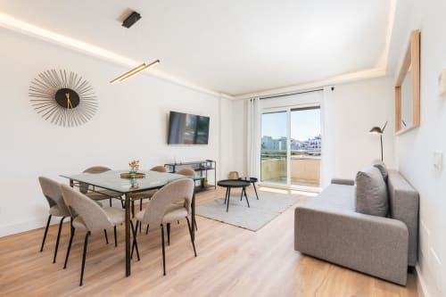 Modern Marbella apartment with dining table, gray sofa, wall clock, flat-screen TV, and balcony overlooking Puerto Banús
