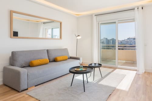 Modern living room at Marbella Home Rentals Marina Banús apartment with gray sofa, yellow pillows, and city view from balcony