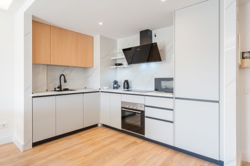 Modern kitchen in Marina Banús apartment with wood cabinets, marble backsplash, black appliances, and wooden flooring at