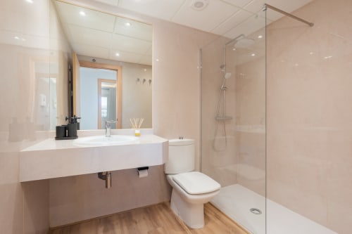 Modern bathroom in Marbella apartment with white sink, toilet, walk-in shower, and wood flooring
