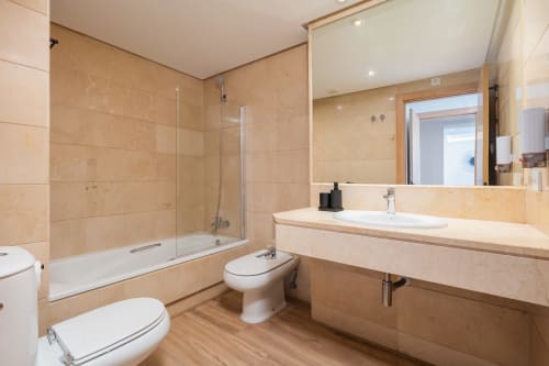 Modern bathroom in Marina Banús apartment with beige marble tiles, walk-in shower, dual sink vanity, and wooden flooring